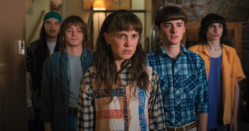 Na imagem, Millie Bobby Brow, personagem Eleven, aparece com seus amigos em roupas da década de 80 surpresos.