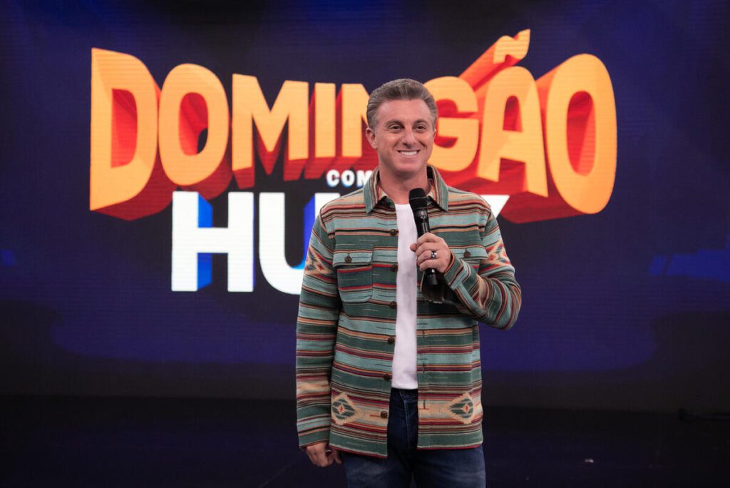 Luciano Huck à frente do logotipo do Domingão, da TV Globo