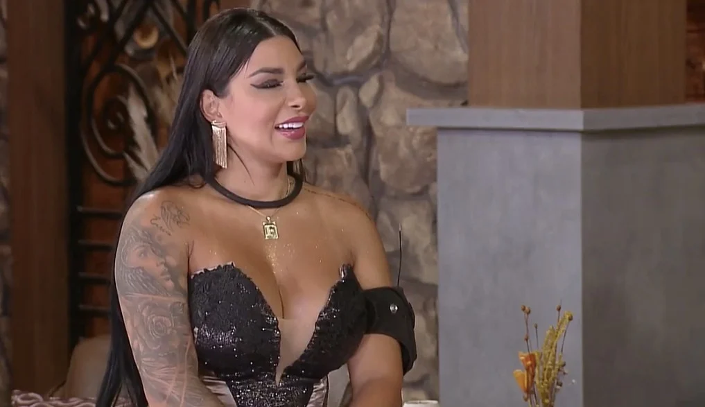 Jenny Miranda está de vestido preto e sorridente olhando para o lado.