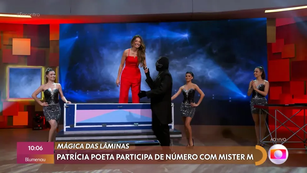 Patrícia poeta usa uma roupa vermelha e está em pé de mãos dadas com o Mister M