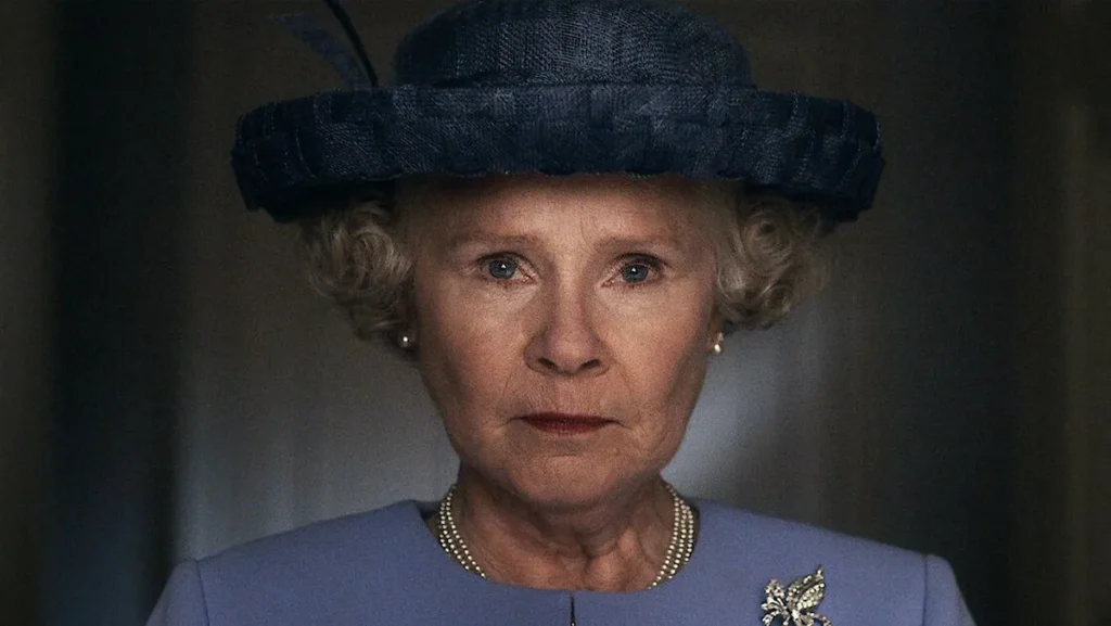 Na imagem, vê-se Imelda Staunton, vestida com blaser e chapéu azul e expressão séria em close.