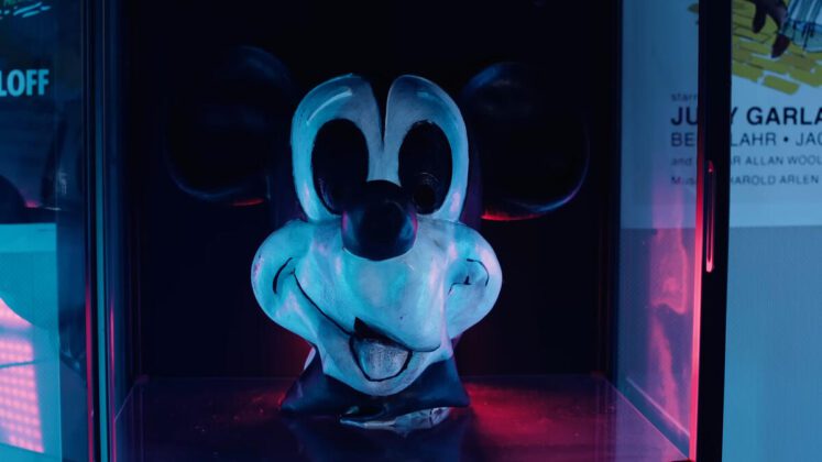 A imagem mostra a cabeça do Mickey Mouse em uma iluminação escura azulada.