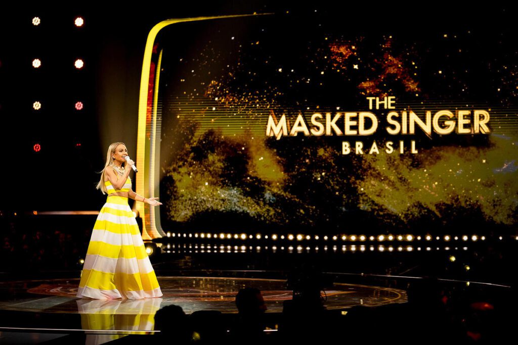 Eliana de vestido amarelo à frente do telão do The Masked Singer Brasil