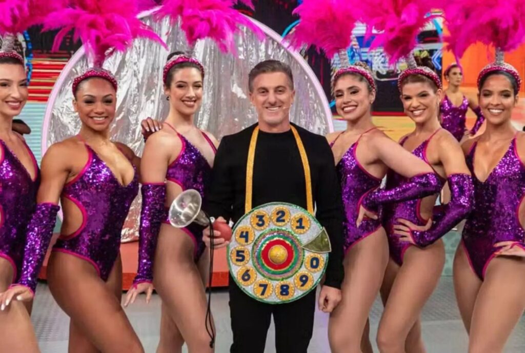 Luciano Huck vestido de Chacrinha rodeado por bailarinas
