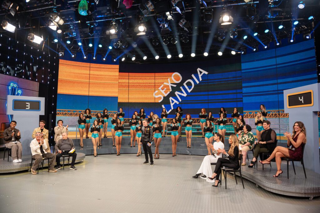 Luciano e elenco à frente do logo do Sexolândia
