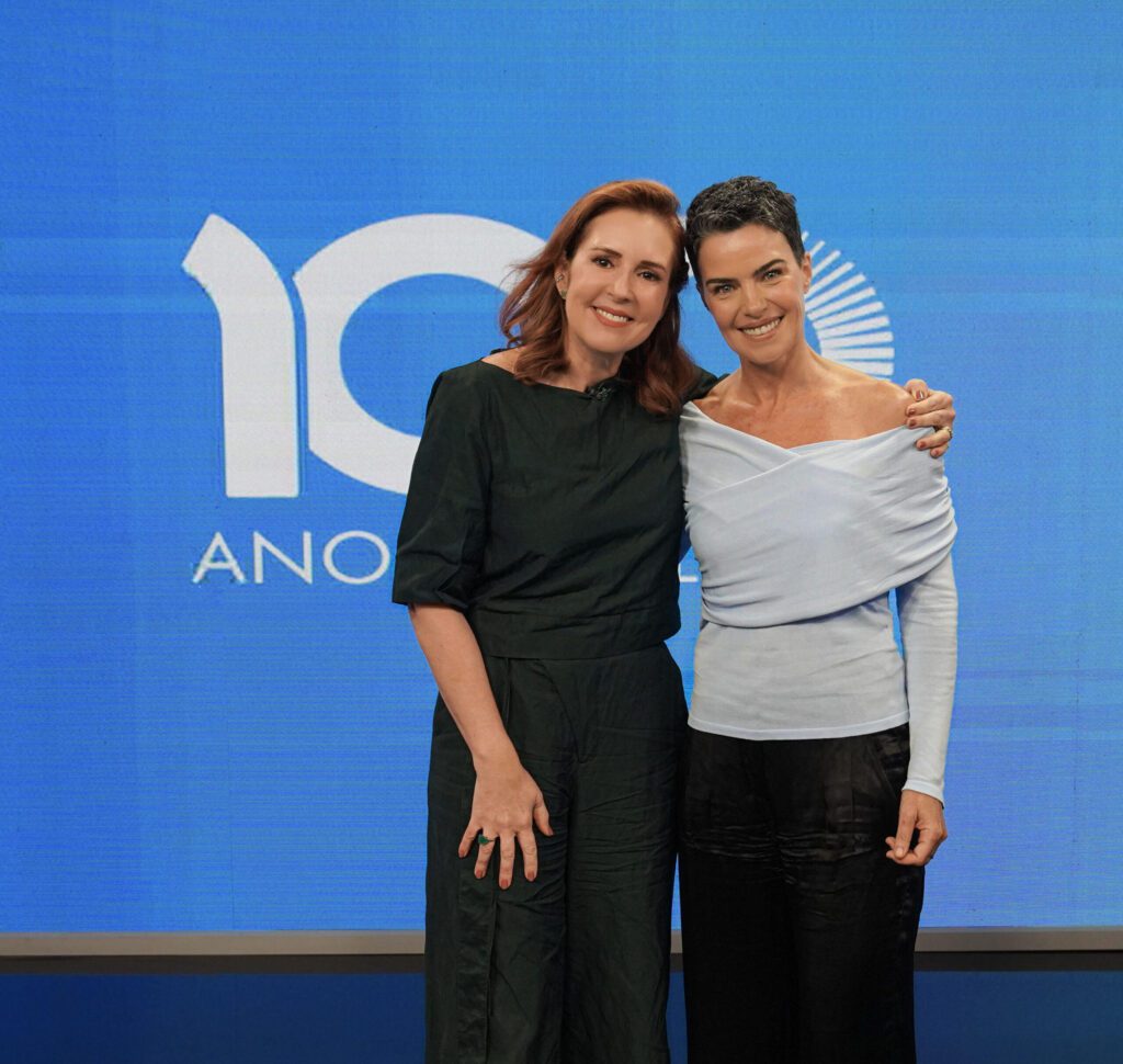 Renata Capucci e Ana Paula Arósio à frente do cenário azul com logo dos 100 anos do grupo Globo