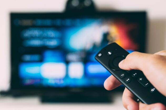 Mão com controle remoto e TV ao fundo