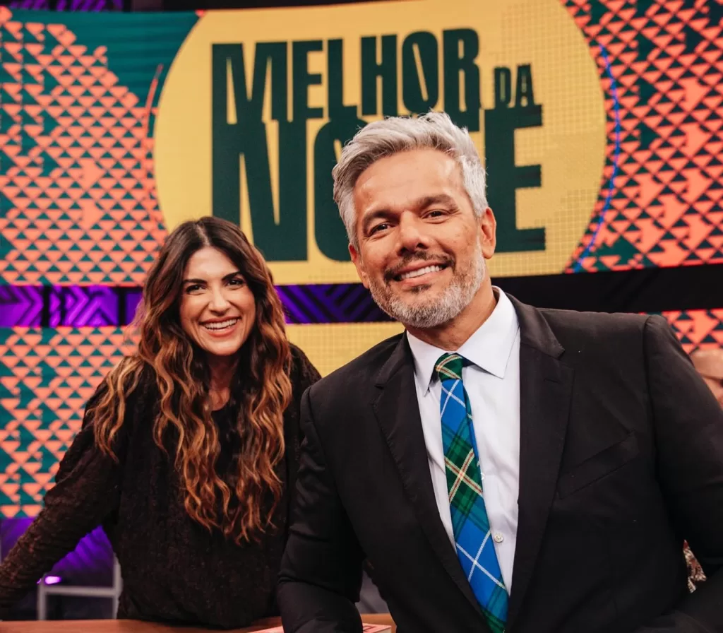Pâmela Lucciola e Otaviano Costa à frente do logo do Melhor da Noite