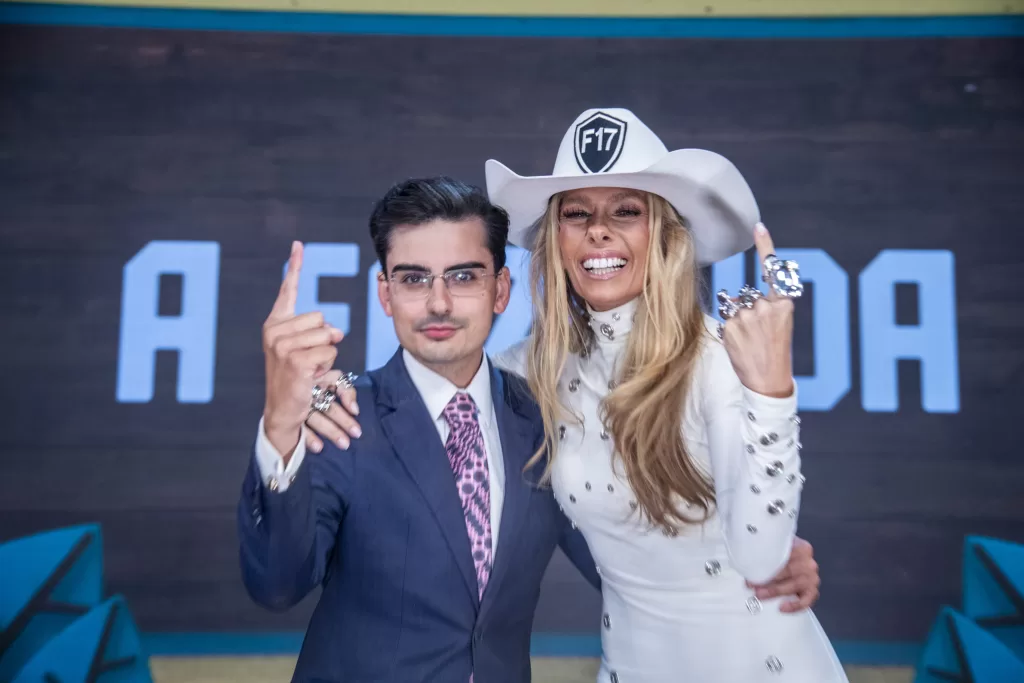 Adriane Galisteu e Dudu Camargo à frente da logo de A fazenda