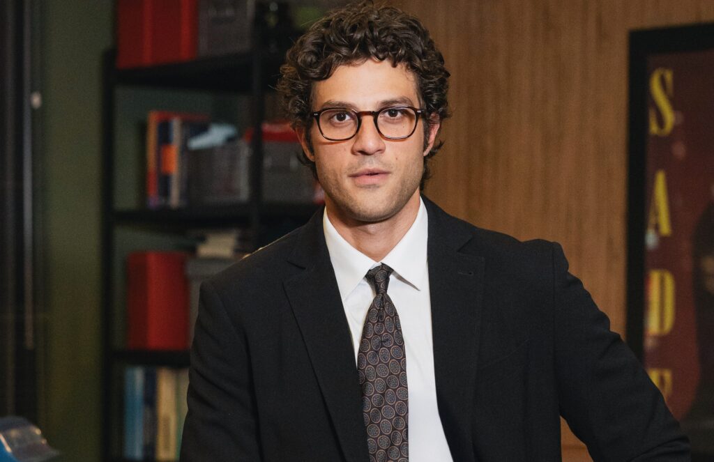 Chay Suede como Pedro. Ele está no escritório, cenário de Quem Ama Cuida